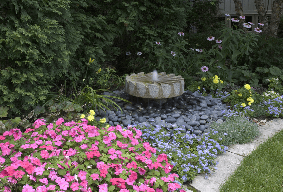Lake Bluff IL granite millstone fountain with Mexican black pebbles and impatiens installed by Van Zelst, Inc.