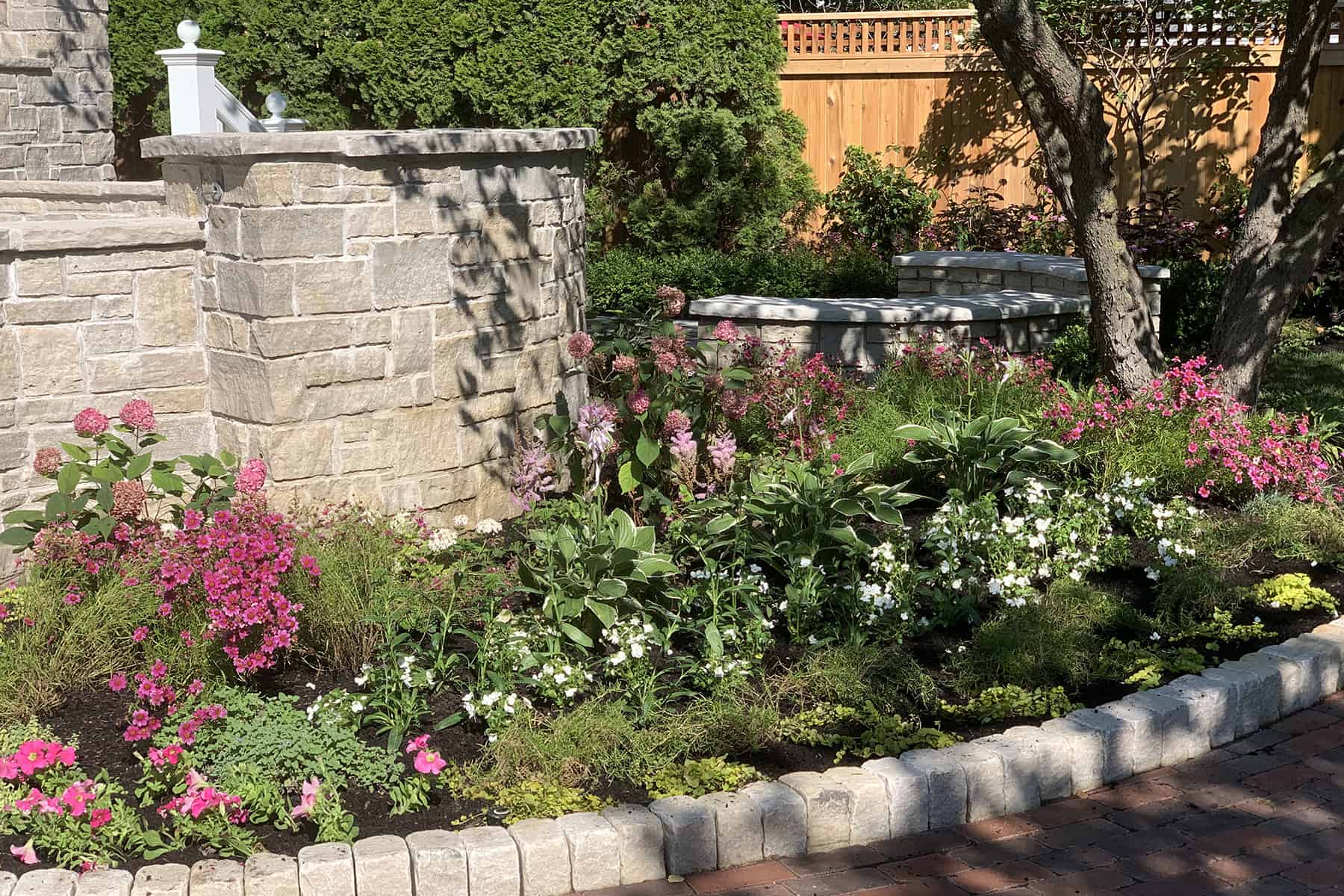 curved planting bed filled with colorful annuals and perennials with stone wall in the background